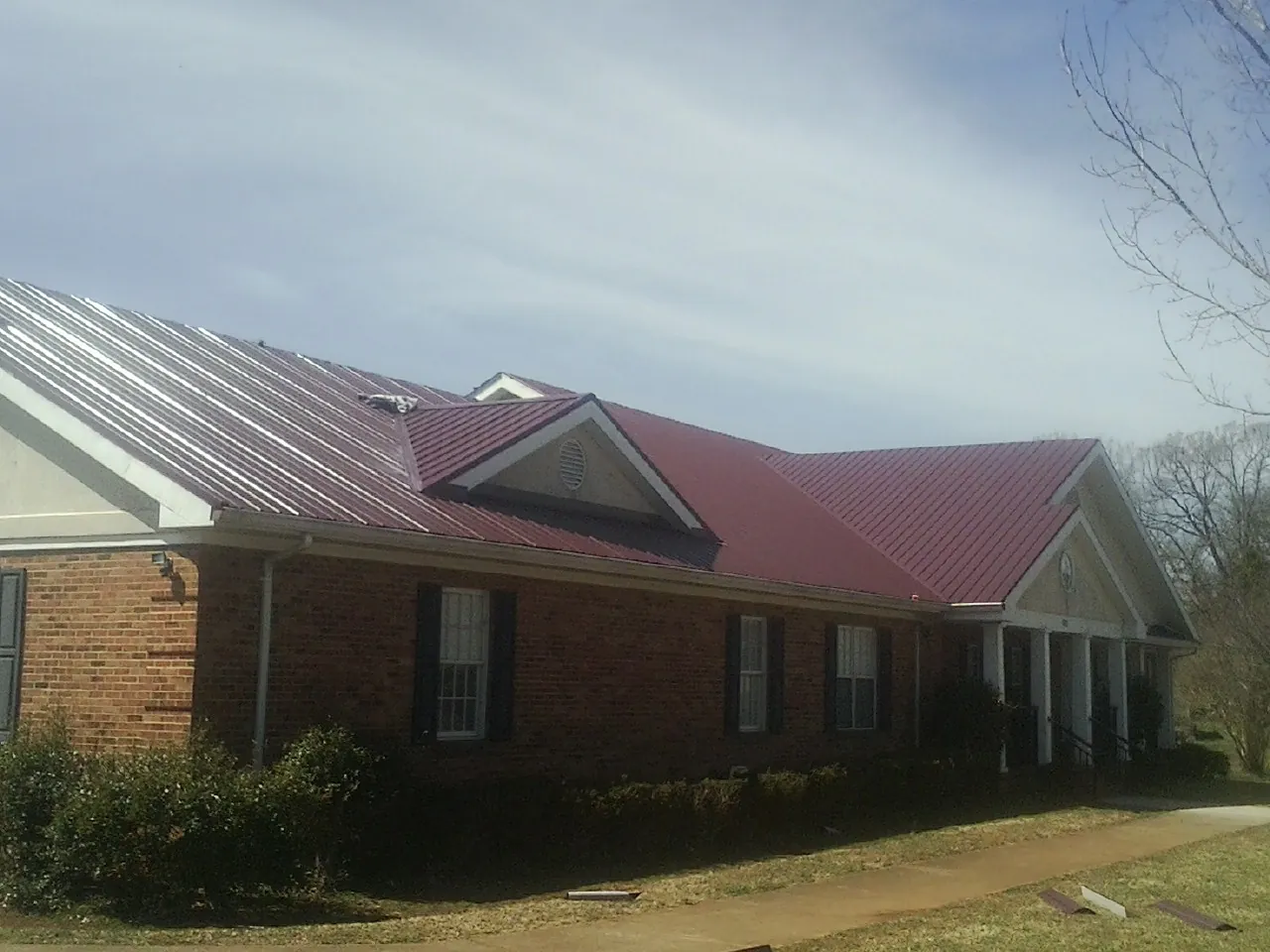 Red metal roof with gabled entries on a long brick building, from a Hail Damage Roof Repair job in Cynthiana