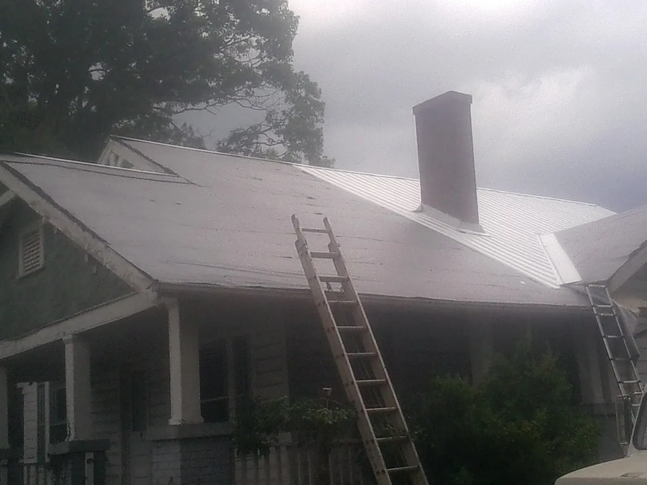 Ladders against a metal roof on an older home with a brick chimney in Cynthiana