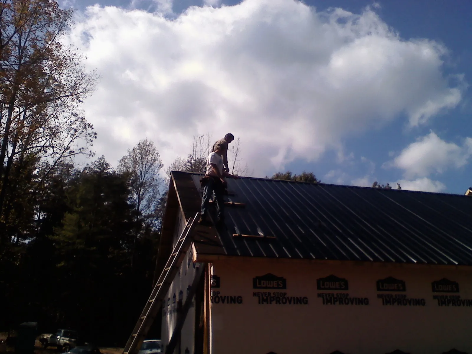 Roofer fastening dark metal panels high against a cloudy sky, from a Roof Inspection job in Cynthiana