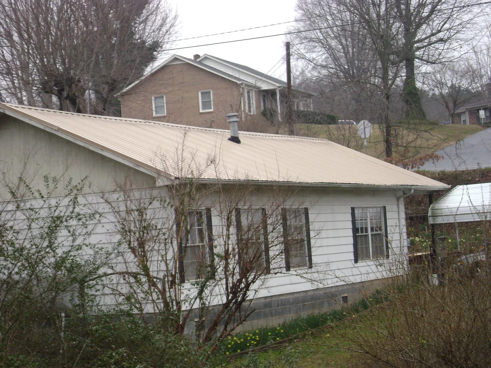 Tan metal roof on a white sided house set into a hillside — Commercial Roofing by Roofing Brothers in Cynthiana